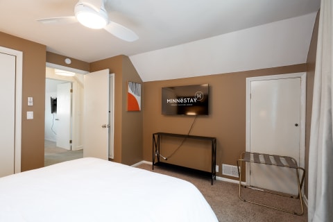 A comfortable bedroom with a TV, a bed, and an abstract painting.