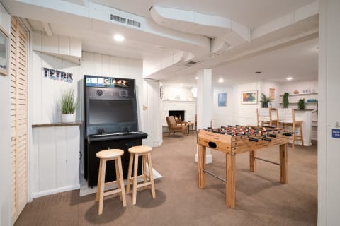 A game room with an arcade machine, foosball table, and seating near a fireplace.