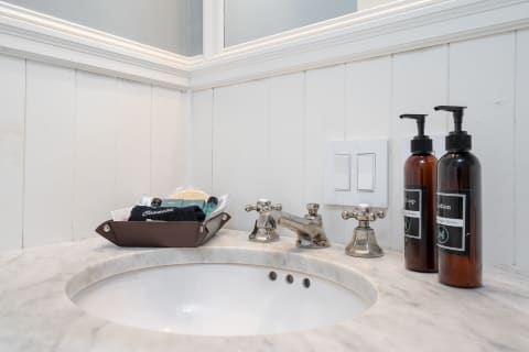 Bathroom counter showcasing marble sink with vintage faucet and toiletries in a tray.