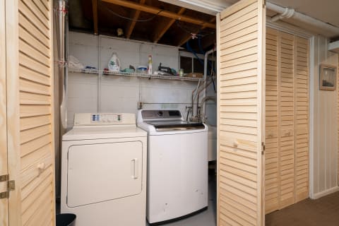 A basement laundry room with a washing machine, dryer, and shelf stocked with laundry supplies.