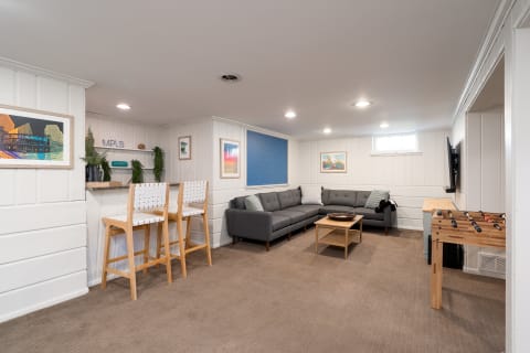 Modern basement living area with a sectional couch, bar area, and foosball table.