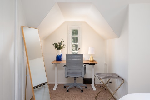 A minimal office space under an a-frame ceiling with a desk, chair, mirror and plant.