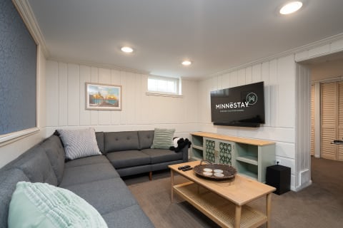 A cozy living room featuring a gray sectional sofa, decorative coffee table, and a mounted television displaying a vacation rental logo.