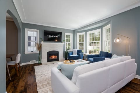 Cozy living room with a white sofa, navy blue chairs, a fireplace, and large windows.