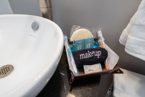 A bathroom with a modern sink and a basket of toiletries including a towel labeled 'makeup'.
