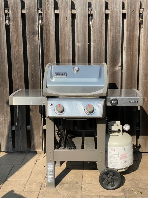 Weber gas grill with propane tank in an outdoor setting near a wooden fence.
