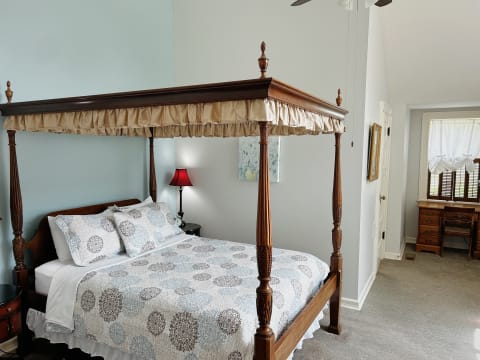 A beautifully decorated bedroom with a four-poster bed, patterned quilt, and warm lighting.