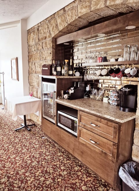 Rustic kitchen bar area with stone walls, wine bottles, and coffee maker, featuring an ornate carpet underneath.