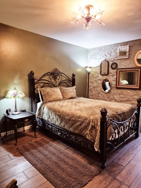 A cozy vintage-style bedroom with an ornate iron bed, warm lighting, and eclectic mirrors on the walls.