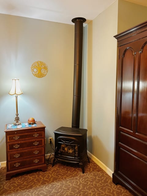 A cozy corner with a wood-burning stove, antique bedside table, and decorative wardrobe in a softly lit room.