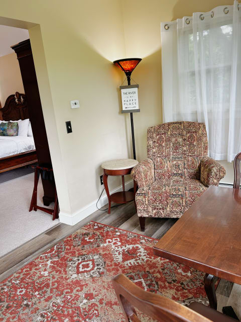 A warm and inviting reading corner featuring a patterned armchair, a lamp with an amber shade, and sheer curtains filtering natural light.