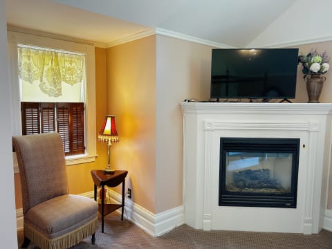 A corner of a cozy room with an armchair, lamp, fireplace, and a TV.