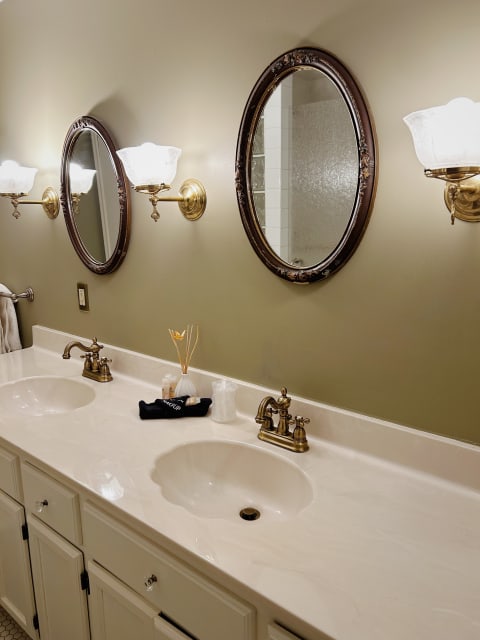 Dual-sink bathroom vanity with brass fixtures and ornate mirrors against olive green walls.
