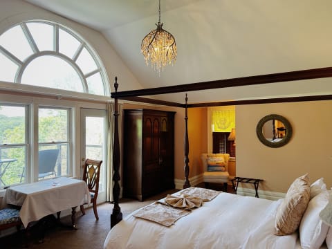 An elegant bedroom featuring a four-poster bed, large arched windows, and warm wooden decor.