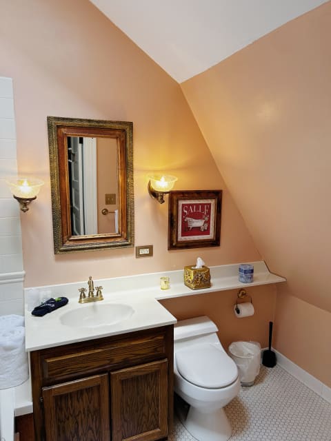 Interior view of a cozy bathroom featuring peach walls, a wooden vanity, and decorative mirror.