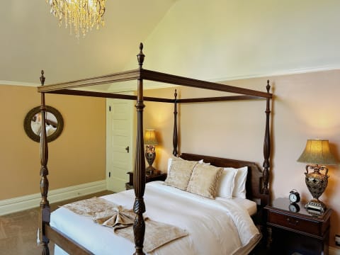An elegant four-poster bed with white linens and plush pillows, accompanied by decorative nightstands and a sparkling chandelier.