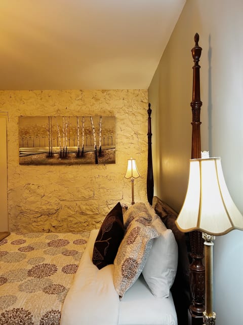 Cozy bedroom corner featuring a four-poster bed with decorative pillows and warm lighting.