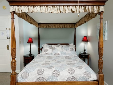 A beautifully decorated bedroom featuring a four-poster bed with intricate wood carvings and cozy bedding, complemented by elegant red lamps.