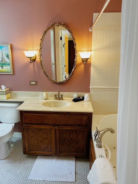 A stylish vintage bathroom featuring a golden oval mirror, warm lighting, and a creamy marble countertop.