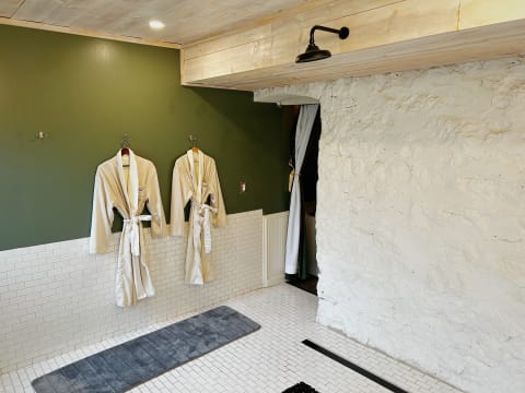 A serene spa room with green walls, white stone, hanging bathrobes, and a soft mat.