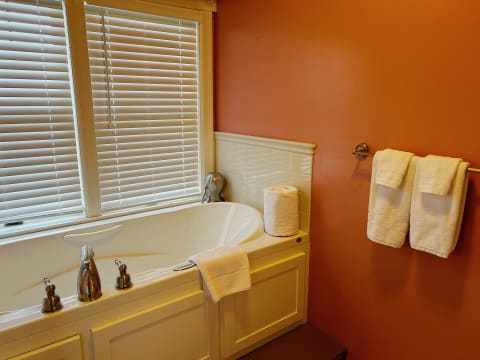 A serene bathroom featuring a stylish soaking tub, warm orange walls, and neatly arranged soft towels.