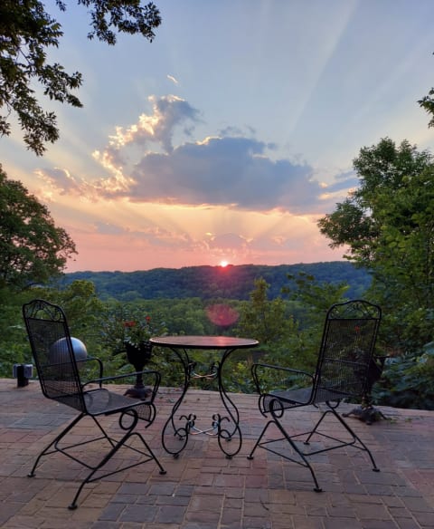 View from a patio with two chairs, overlooking hills at sunset with colorful skies.