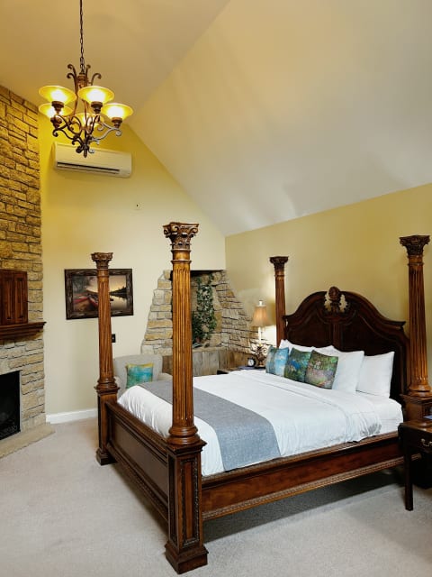 Luxurious bedroom with a four-poster bed, stone fireplace, and elegant chandelier.
