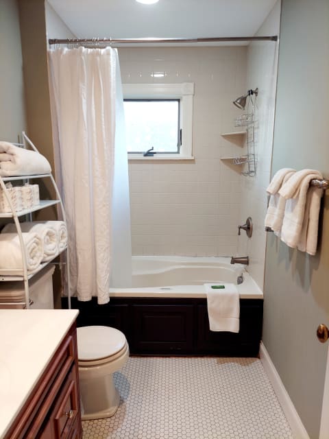 A private bathroom with a tub-shower combo, towels, and soft lighting.