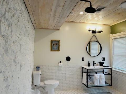 Stylish bathroom with exposed stone walls, wood ceiling, and modern fixtures, showcasing a mix of industrial and contemporary design.