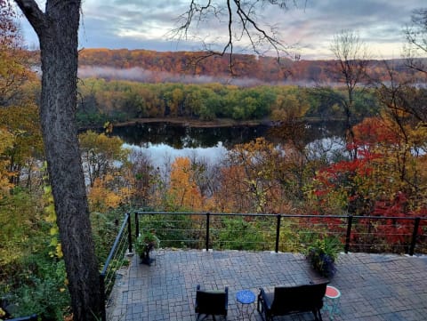 A scenic autumn view of a river surrounded by colorful fall trees from a patio with seating.