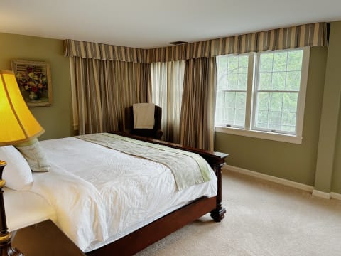 Elegant bedroom with a large bed, soft linens, and window views of greenery.