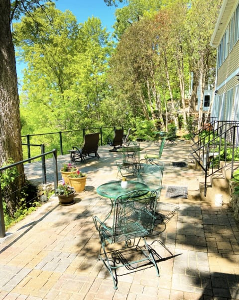 Outdoor patio with metal furniture, surrounded by trees and flowers, in bright sunlight.