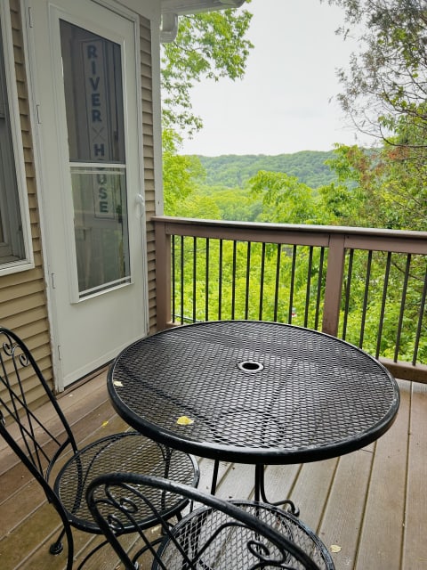 Wrought-iron table and chairs on a private deck overlooking a green forest landscape.