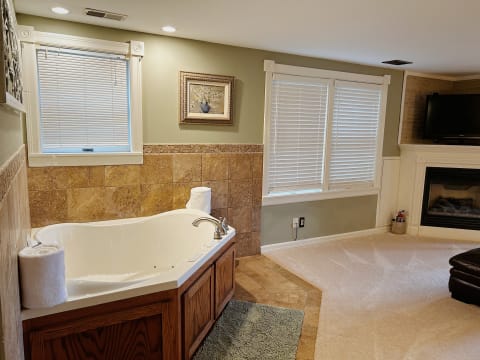 Luxurious bathroom showcasing a jetted tub, travertine accents, and a cozy fireplace.