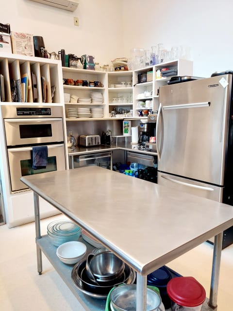A modern kitchen with stainless steel prep table, organized shelves of dishes and appliances.