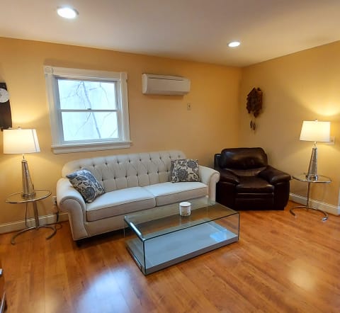 Cozy living room featuring a tufted white sofa, leather armchair, glass coffee table, and warm lighting.