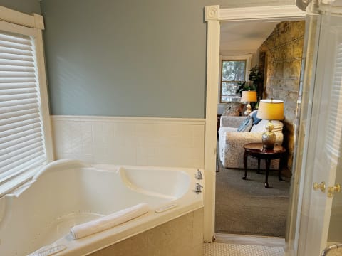 A jetted tub in a serene bathroom, leading to a cozy seating area with a stone wall.