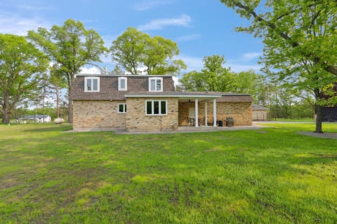 Side view of a brick house with a covered porch in a green landscape.
