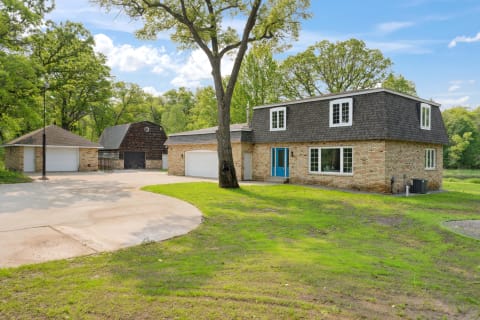 A beautiful house featuring a blue door, brick exterior, and surrounding greenery.