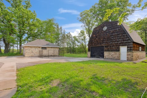 Brick building and wooden barn in a green landscape with a blue sky.