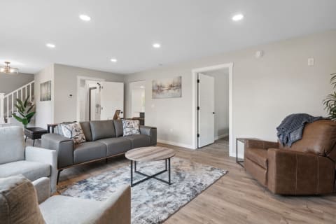 Modern living room featuring a gray leather sofa, light gray armchairs, a wooden coffee table, and decorative pillows.