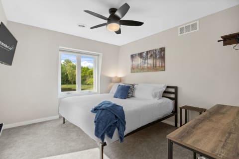 Modern bedroom with a bed, desk, and window overlooking trees.