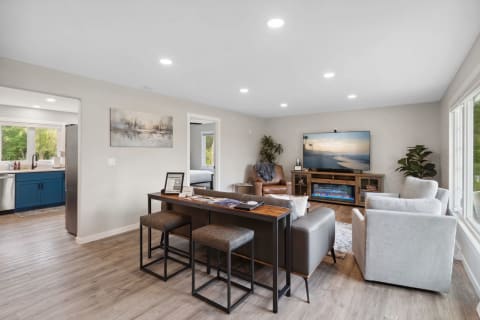 Contemporary living room with a gray sofa, wooden entertainment unit, and blue kitchen cabinetry visible.