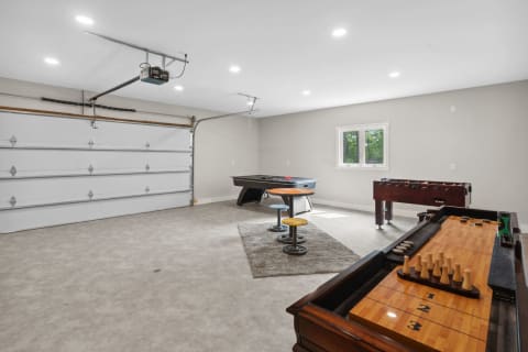 Spacious garage game room with a pool table, foosball table, and colorful stools on a gray rug.