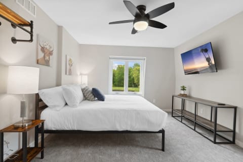 A stylish bedroom with a bed, lamps, and a TV, showcasing animal portraits on the wall.