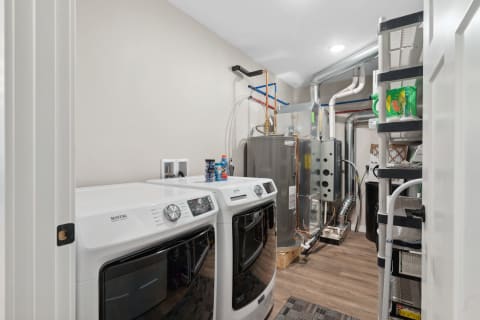 Modern laundry room featuring white Maytag washing machines, a silver water heater, and organized storage.