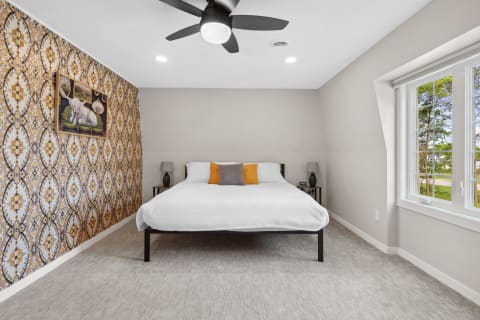 Modern bedroom featuring a queen-sized bed with accent pillows and patterned wallpaper.