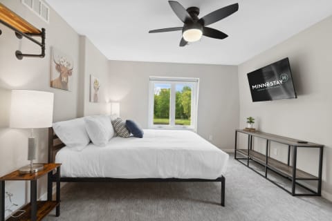 Modern bedroom with a bed, lamps, and a view of greenery.