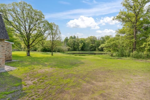 Outdoor landscape with green grass, trees, and a pond under a clear sky.