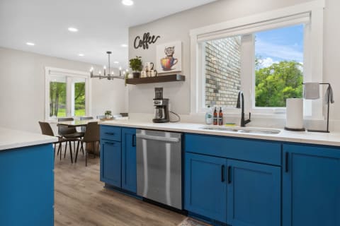 Bright and modern kitchen with blue cabinetry and a large window overlooking the outdoors.